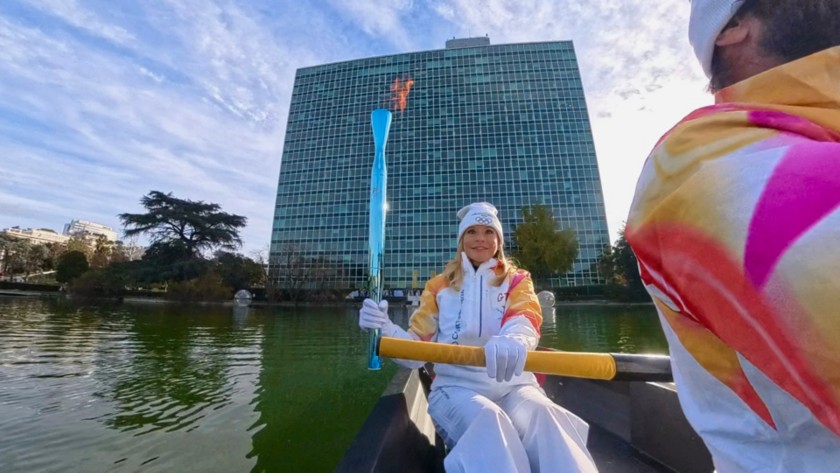 Davanti al palazzo di Vetro Eni, la Torcia Olimpica viene trasportata da un tedoforo su una canoa 