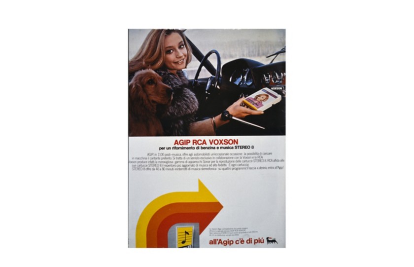 Raffaella Carrà at the wheel with the yellow, orange, and red arrow from the Agip advertising campaign below
