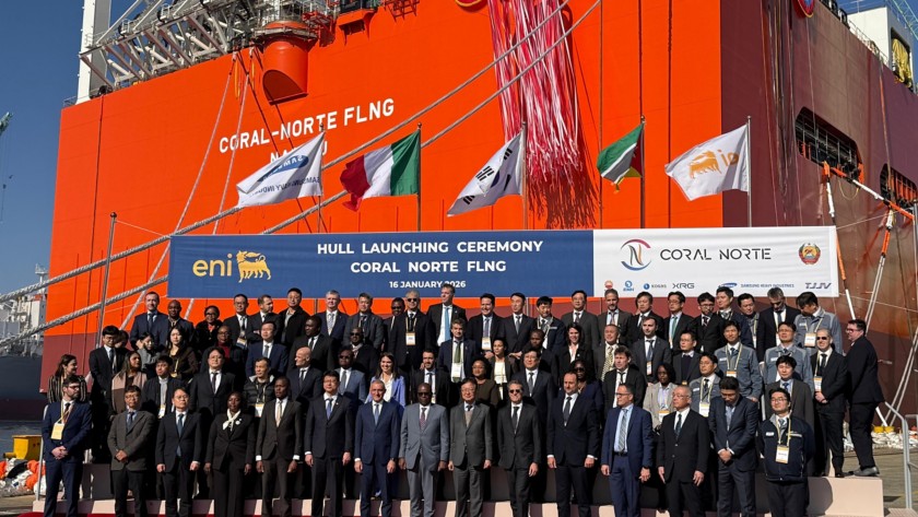 Group photo of authorities, executives and industrial partners at the Coral Norte FLNG hull launching ceremony, standing in front of the orange facility structure with the official Eni banner and international flags.