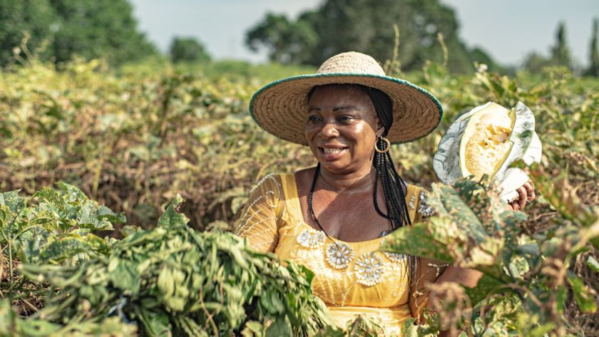Donna africana sorride in un campo agricolo tenendo in mano il frutto
