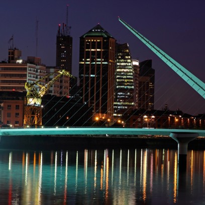 Skyline notturno di Buenos Aires con il Puente de la Mujer illuminato, le luci della città riflesse sull’acqua e gli edifici moderni sullo sfondo del quartiere Puerto Madero