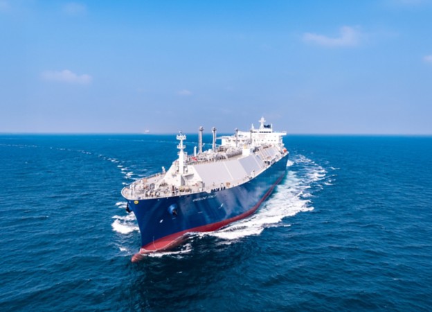 A large liquefied natural gas (LNG) carrier sailing in open sea under a clear blue sky.