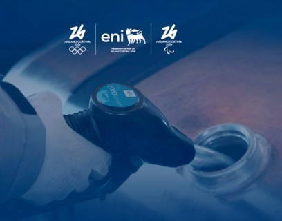 Primo piano di una mano con guanto bianco che impugna l’erogatore di carburante durante il rifornimento; in alto i loghi Milano Cortina 2026 ed Eni, premium partner dei Giochi.