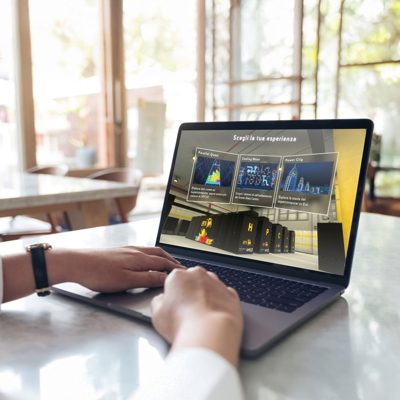 Persona seduta a un tavolo usa un laptop con un’interfaccia digitale che mostra diverse opzioni di esperienza; ambiente luminoso con grandi finestre sullo sfondo.