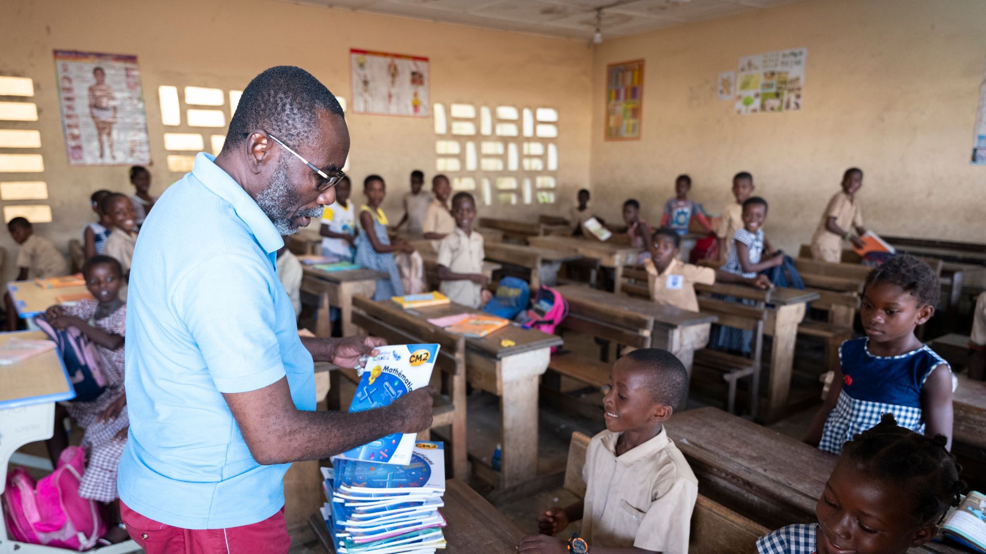 African teacher hands out classroom books to pupils