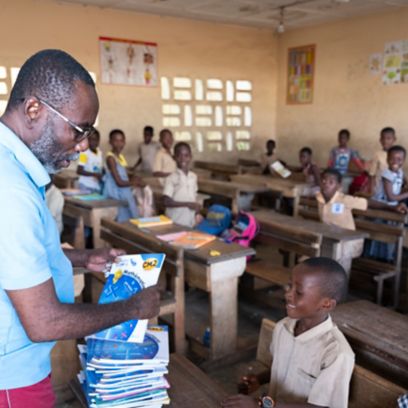 African teacher hands out classroom books to pupils