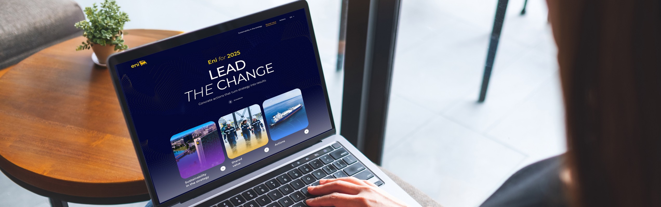 Woman sitting and working on a laptop with the ‘Eni for 2025 – Lead the Change’ website open on the screen