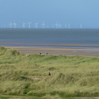 Panoramic photo depicting an English beach with offshore wind turbines on the horizon