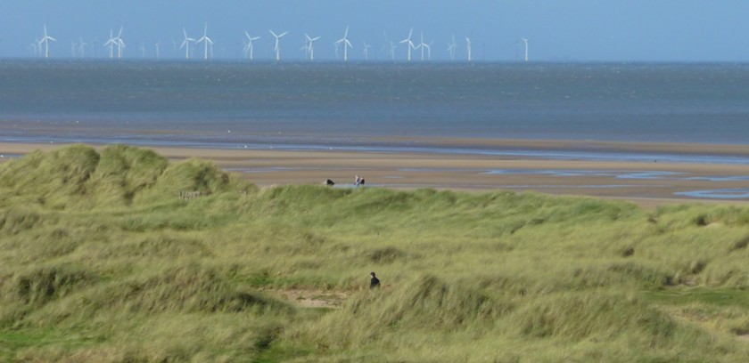 Panoramic photo depicting an English beach with offshore wind turbines on the horizon