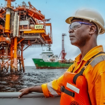 Profile worker on a stationary vessel in front of him, with the Nené field offshore installation in the background