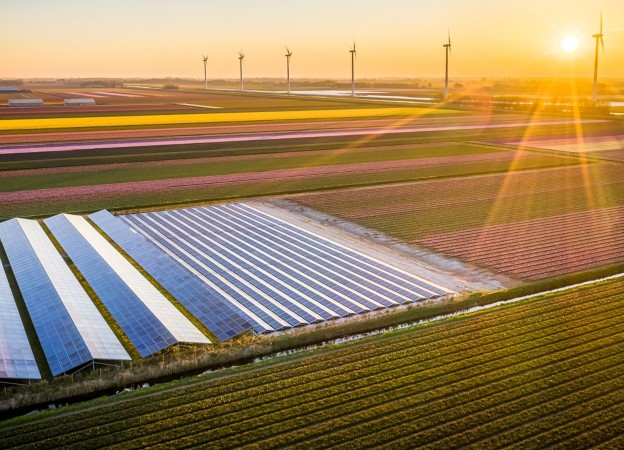 View of solar panels and wind turbines in the field with sunset