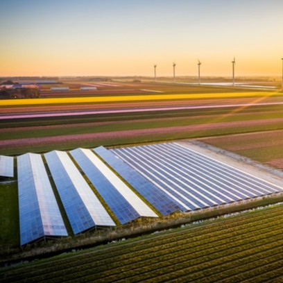 View of solar panels and wind turbines in the field with sunset