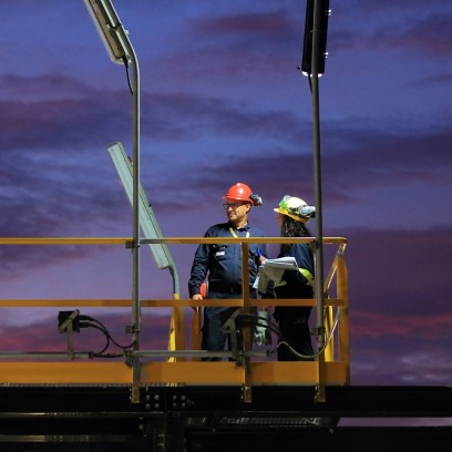 Two workers on the scaffolding of a construction site lit by the sunset