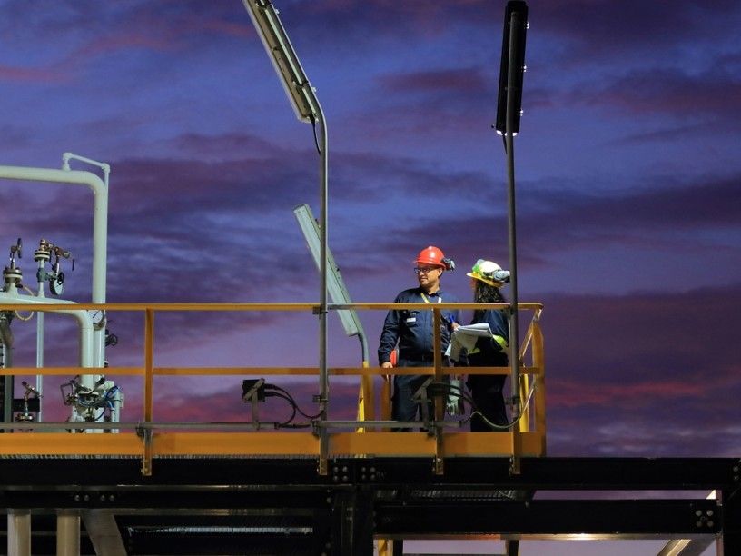 Two workers on the scaffolding of a construction site lit by the sunset