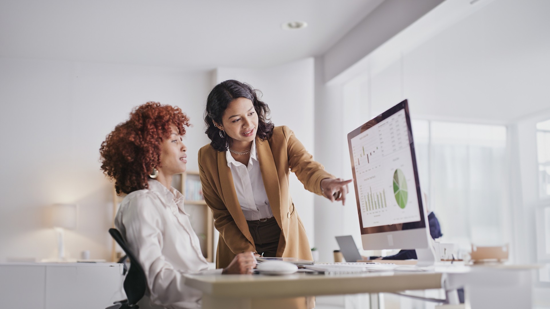 Two female colleagues in the office look at monitor data