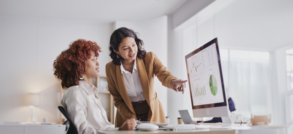 Two female colleagues in the office look at monitor data