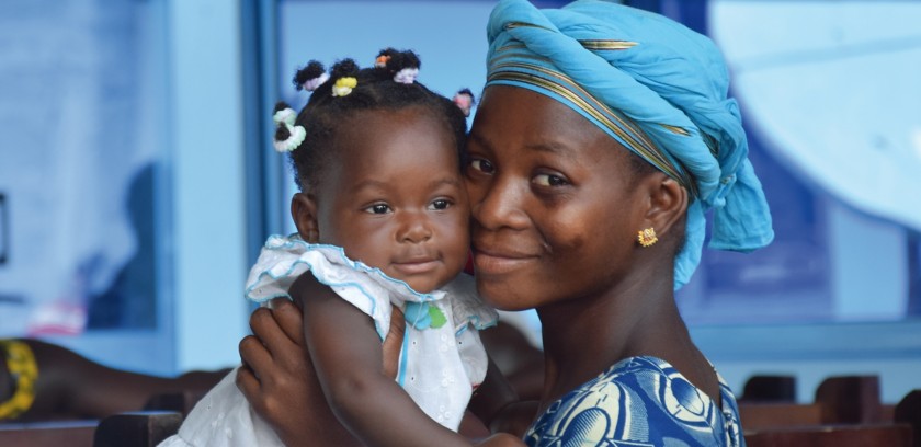 Woman with a blue headdress smiles while holding a little girl in her arms