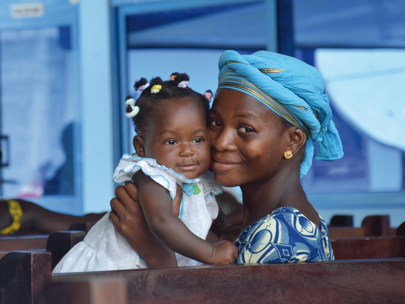 Donna con copricapo azzurro sorride tenendo in braccio una bambina