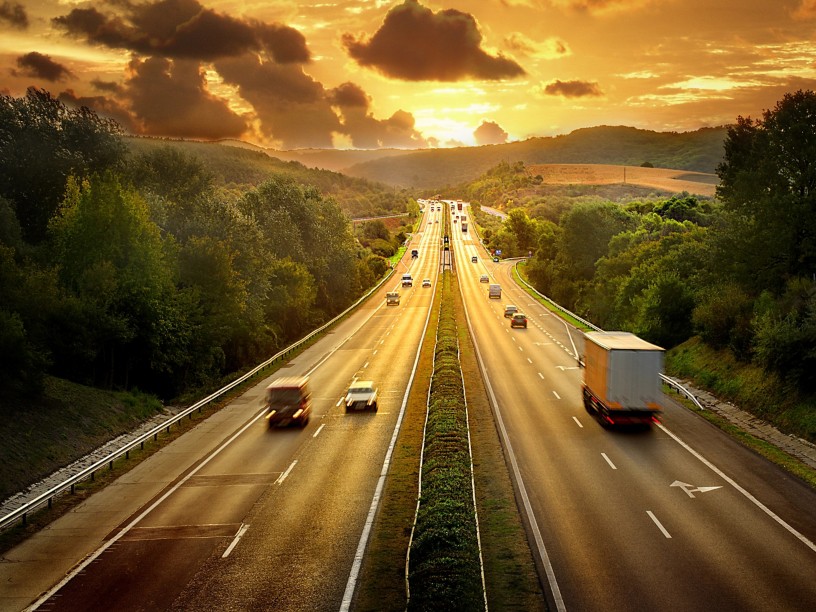 vista di un autostrada al tramonto con automobili e autoarticolati 