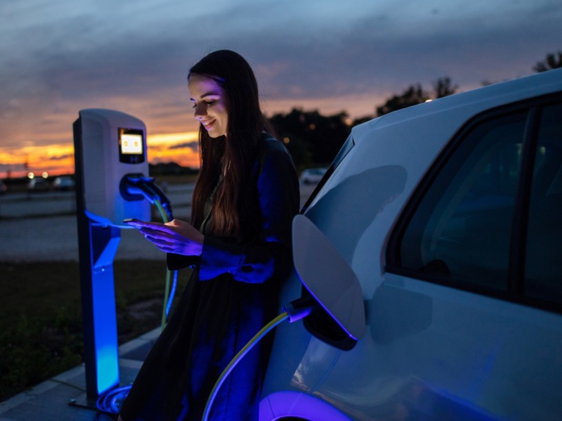 Ragazza guarda il cellulare al tramonto mentre ricarica la macchina elettrica