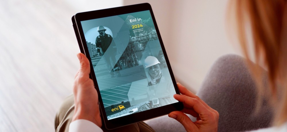 A person holds a tablet displaying Eni’s digital report titled “Eni in Egypt 2024 – Sustainability Local Report.” The cover features overlapping images of engineers and industrial facilities in blue-green tones.