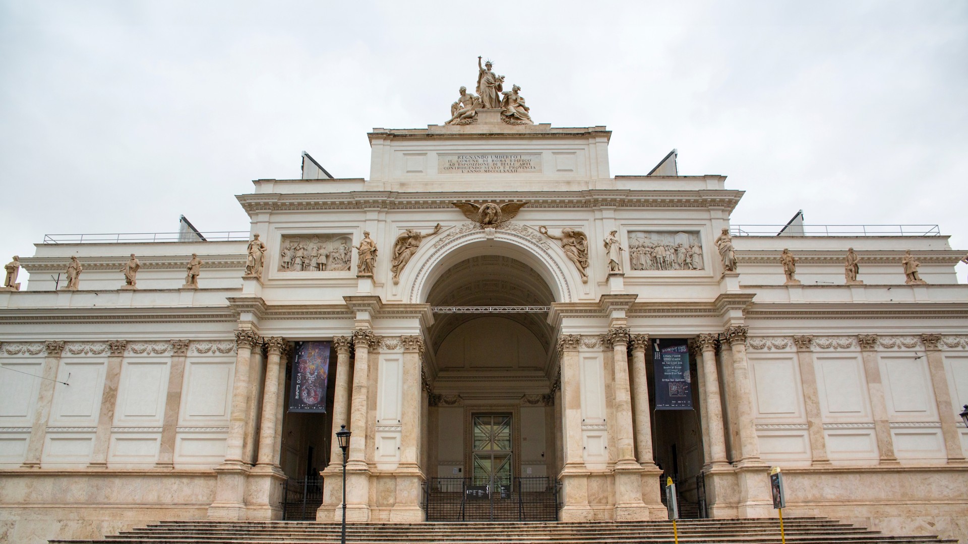 facciata di un palazzo storico in pietra chiara con archi e statue e colonne