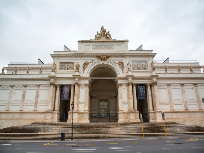 Facade of a historic building made of light-colored stone, featuring arches, statues, and columns