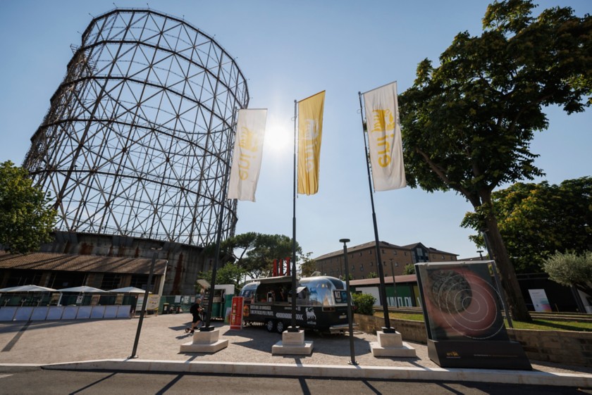 A food truck, Eni flags, and the Gazometro in the background