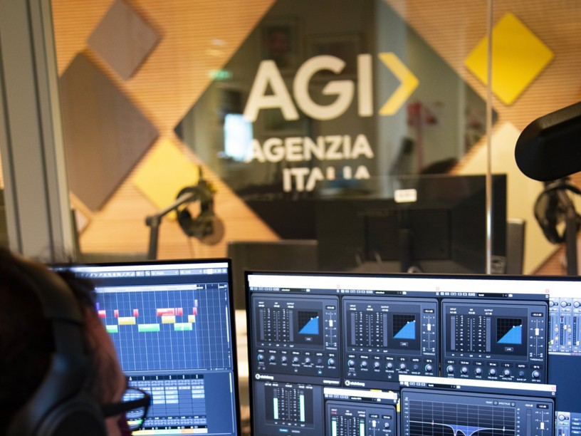 Man with headphones at a computer in a recording studio, with the AGI logo in the background