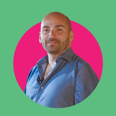 un ragazzo sorridente con i capelli rasati e una camicia blu