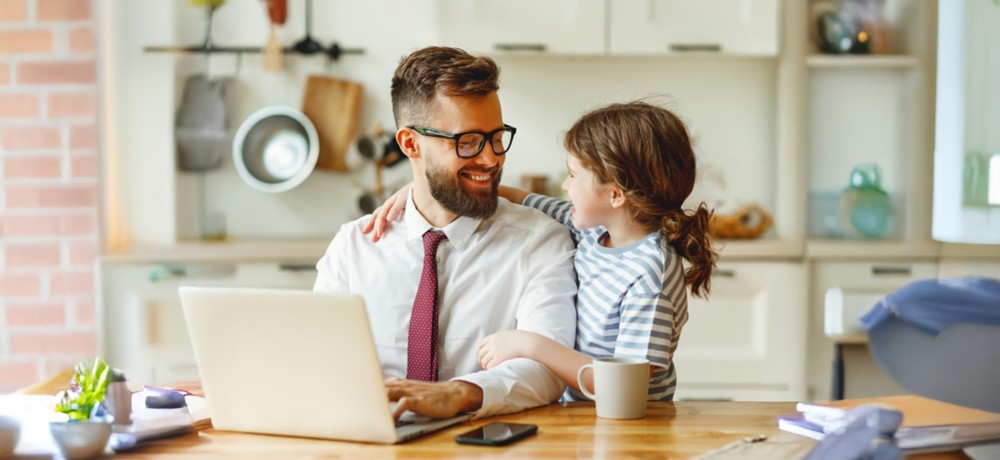 Man sitting at the table in front of a computer with a little girl next to him