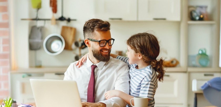 Man sitting at the table in front of a computer with a little girl next to him