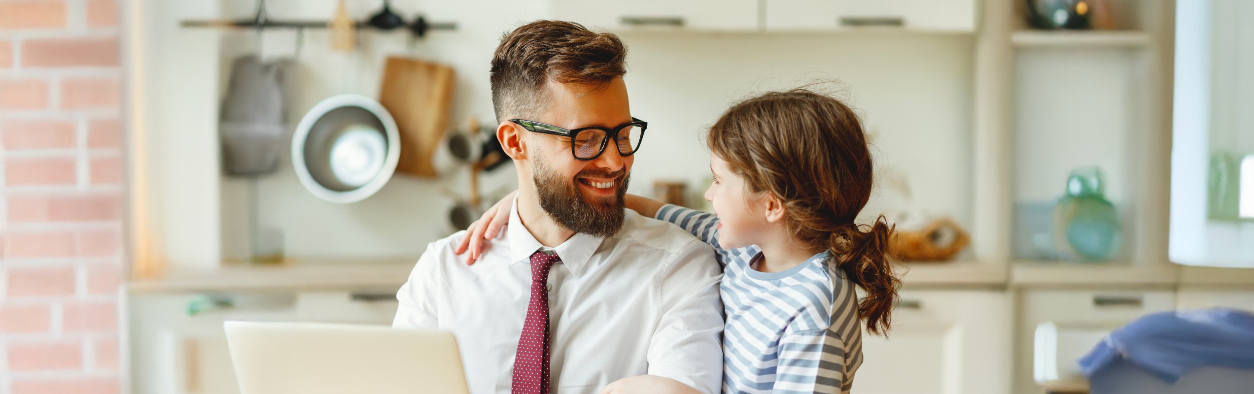 Man sitting at the table in front of a computer with a little girl next to him