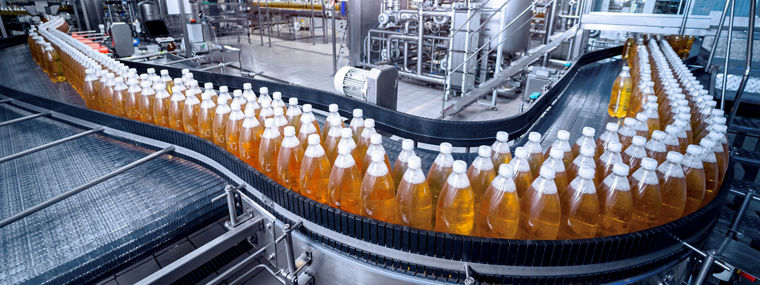 Bottles filled with yellow liquid moving on a curved conveyor belt in a factory.