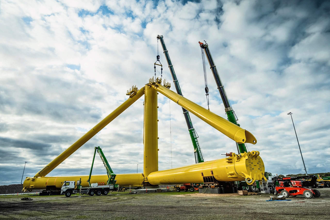 Truck-mounted cranes assemble the steel, yellow-painted base.