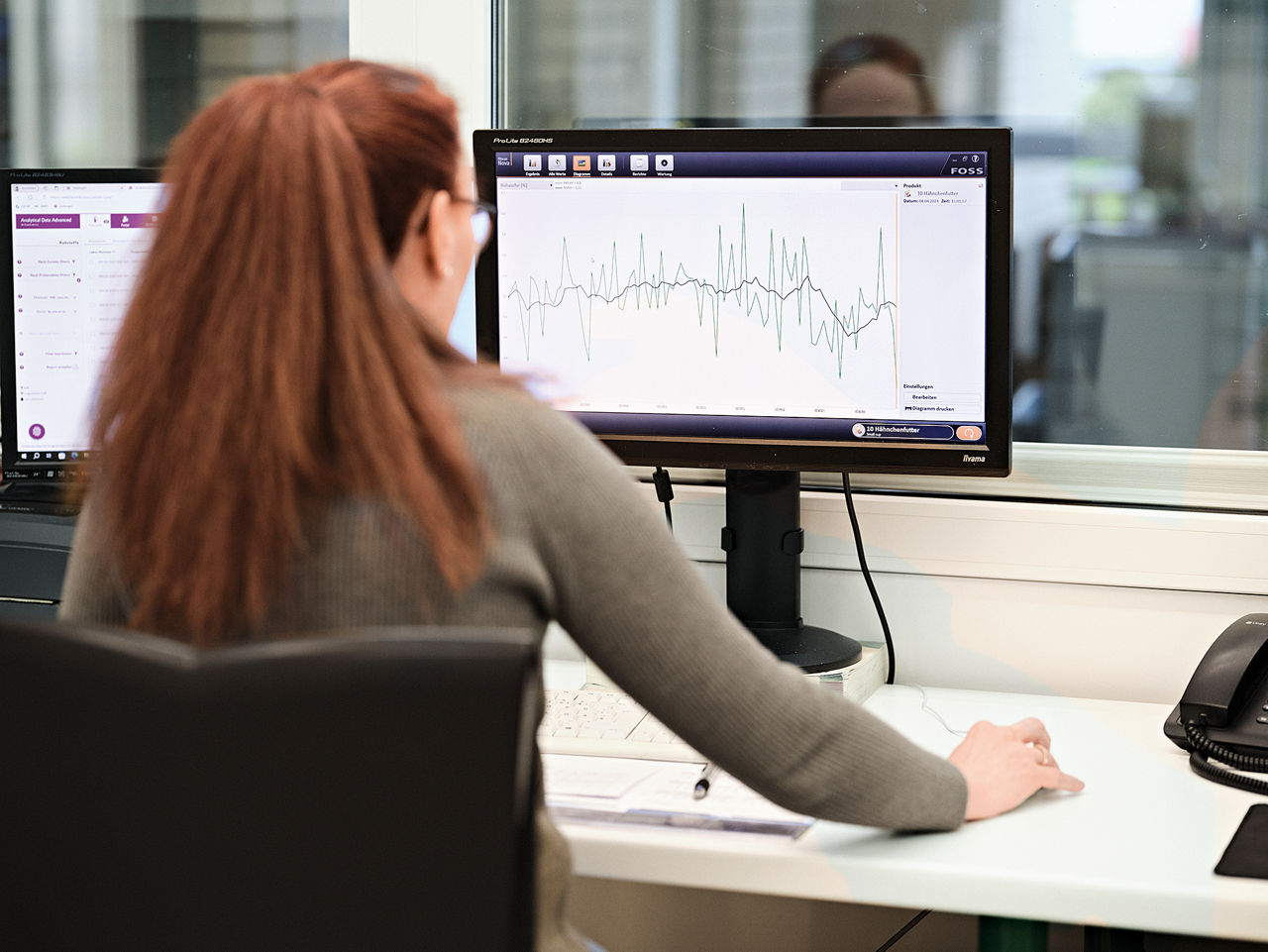 Eine Frau sietzt an einem Computerarbeitsplatz und betrachtet ein Chart auf dem Monitor.