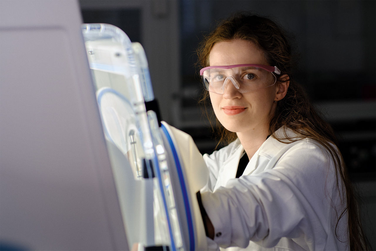 Michelle Dargatz sits in front of a closed container into which she reaches with airtight gloves.