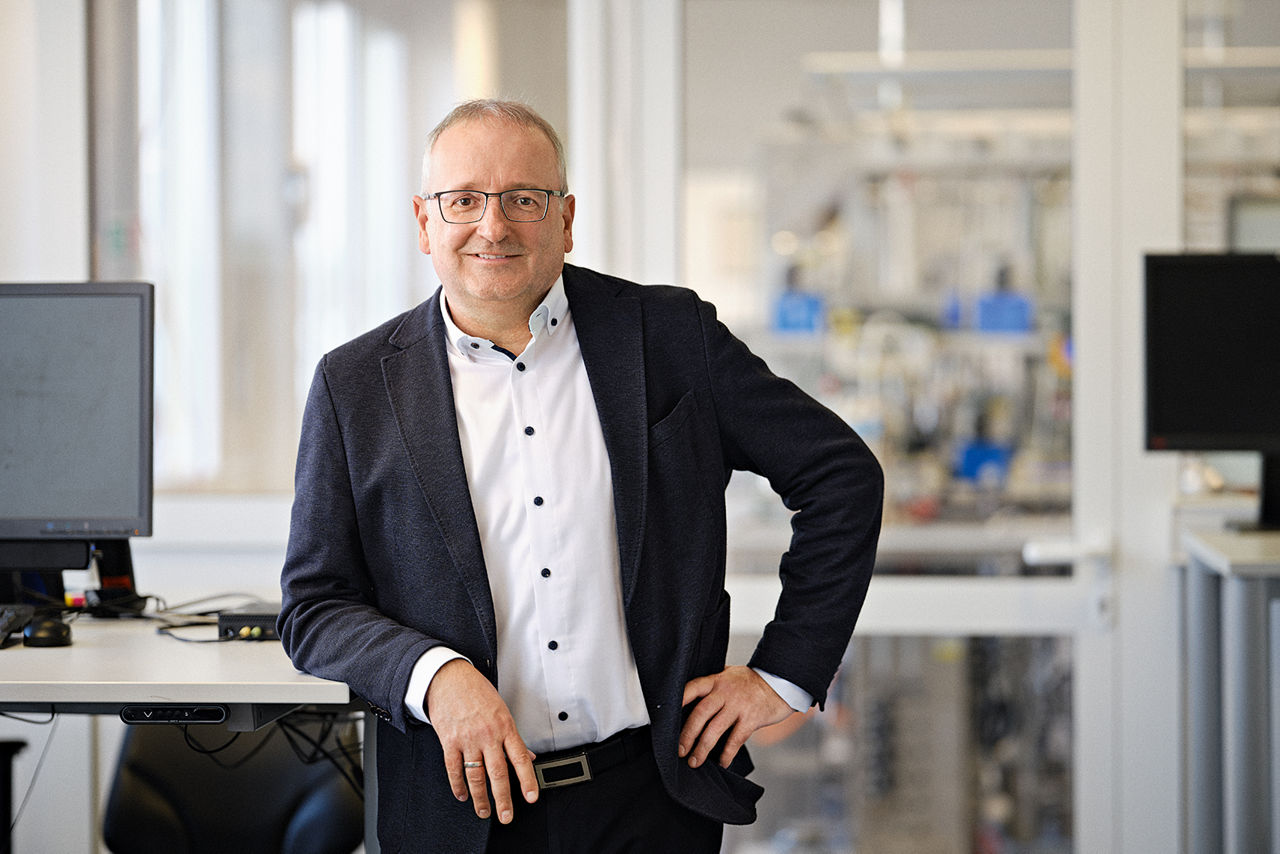 Stefan Pelzer leans on a high table. A laboratory room can be seen behind him.