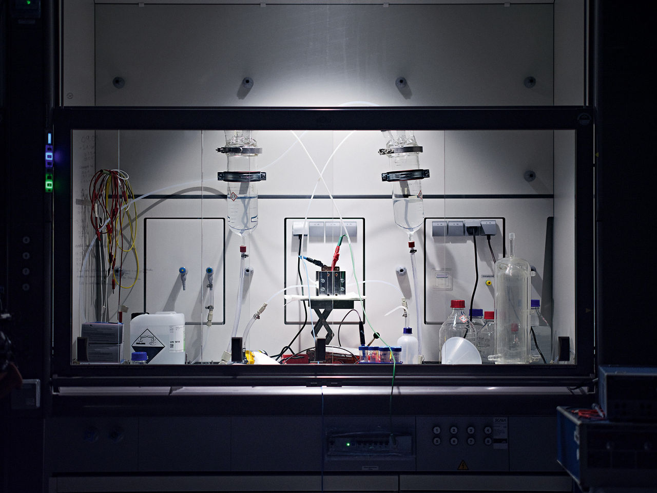 Ein Laborschrank mit Glastüren, in dem ein kleiner Elektrolyseur aufgebaut ist.