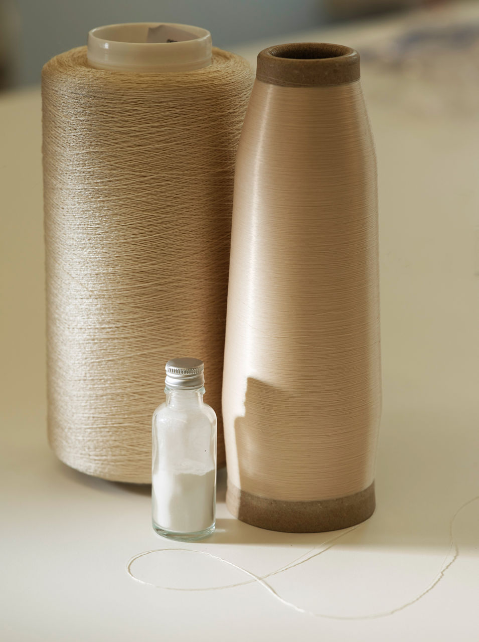Two spools with threads of different thickness behind a vial containing a white liquid