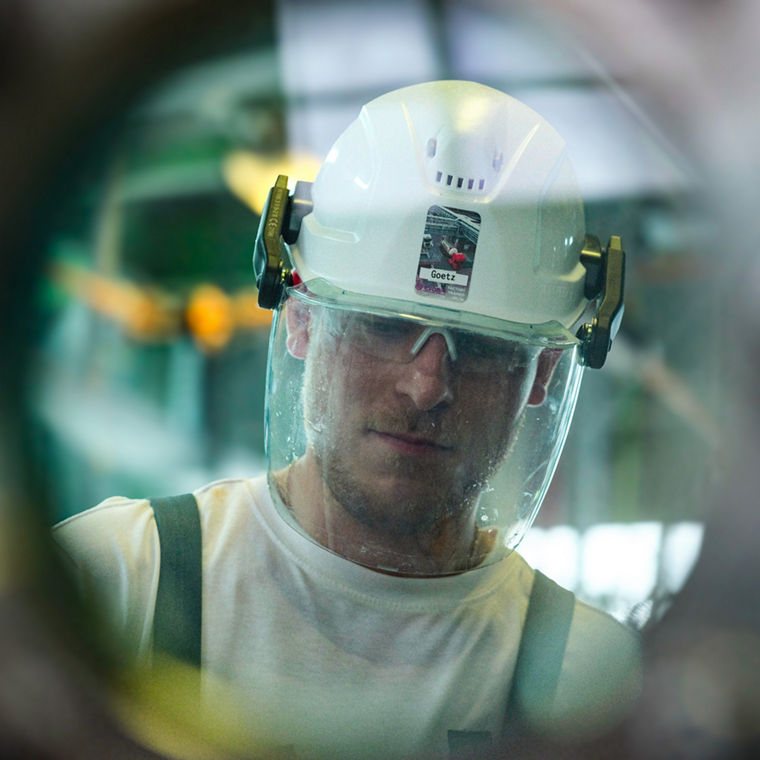 Ein Evonik-Mitarbeiter mit Helm und Schutzbrille schaut durch ein rundes Sichtglas.