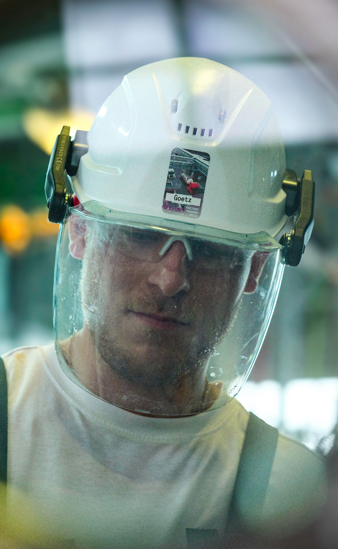 Ein Evonik-Mitarbeiter mit Helm und Schutzbrille schaut durch ein rundes Sichtglas.