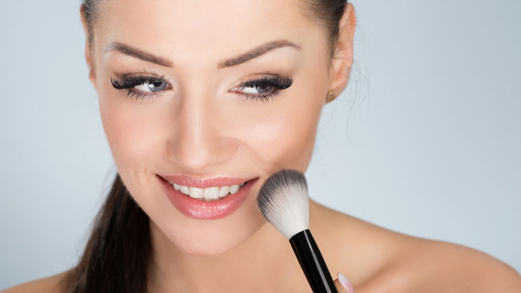 Happy beautiful woman applying face powder