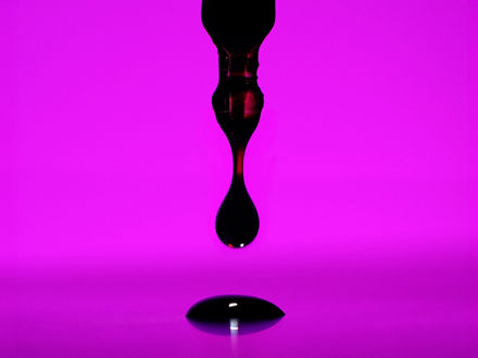 Ein dunkler Tropfen tropf von einer Pipette auf eine purpurfarbene Platte