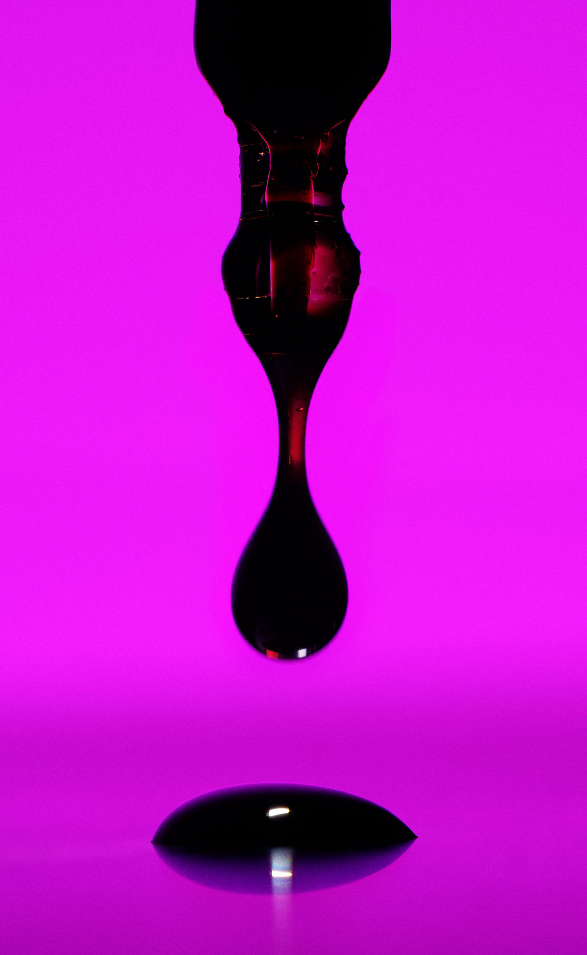 Ein dunkler Tropfen tropf von einer Pipette auf eine purpurfarbene Platte