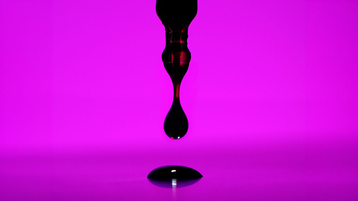 Ein dunkler Tropfen tropf von einer Pipette auf eine purpurfarbene Platte