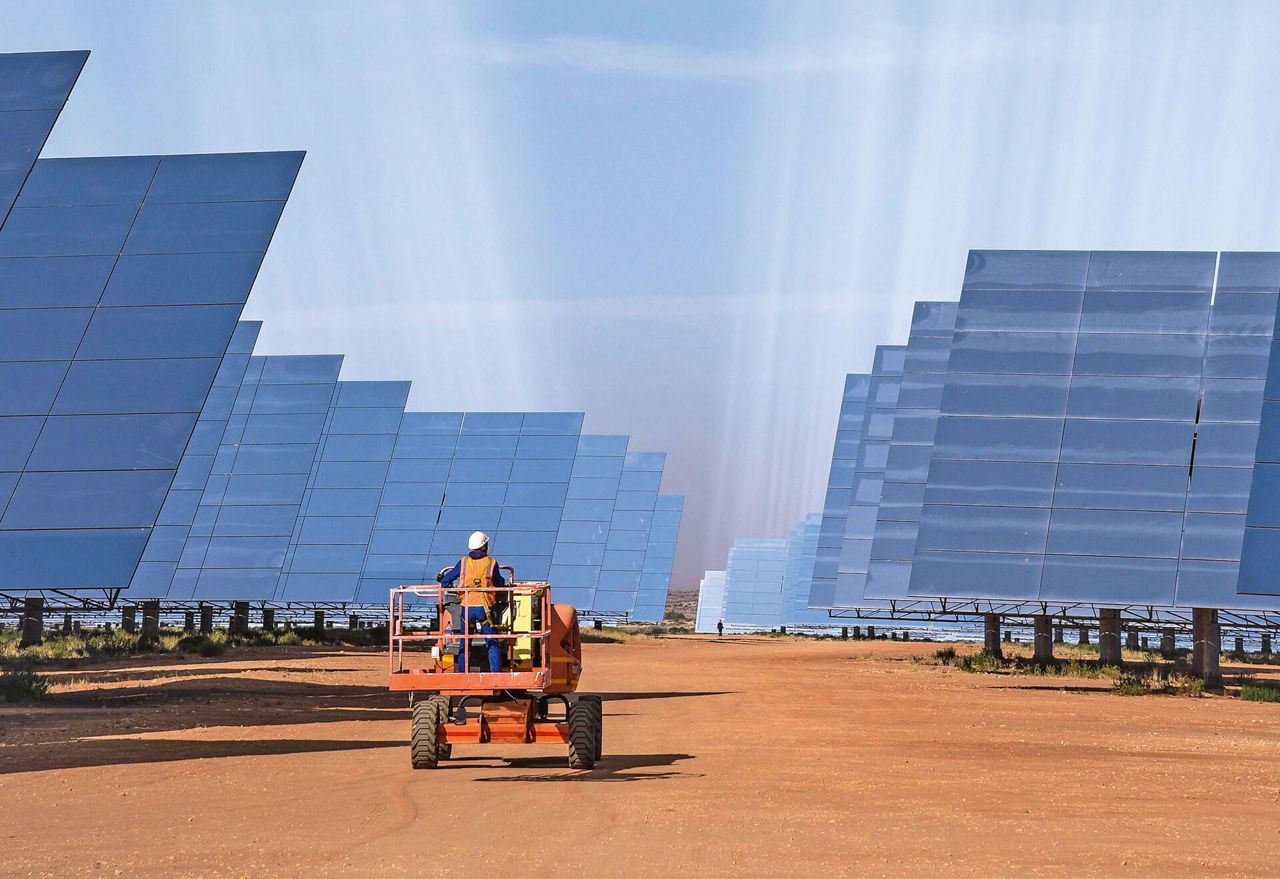 A man stands on a piece of mobile equipment and drives it through a huge solar park.