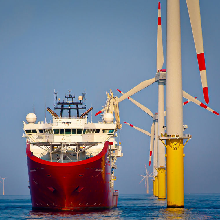 A service ship is moored at sea next to tall wind turbines under construction.