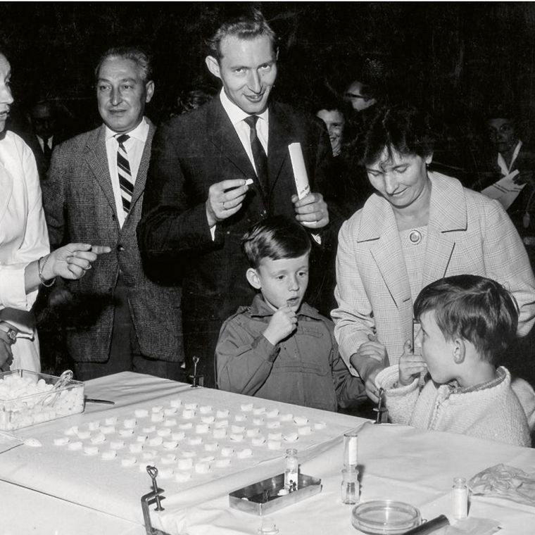 Children and adults stand in line and receive sugar cubes with polio vaccine.