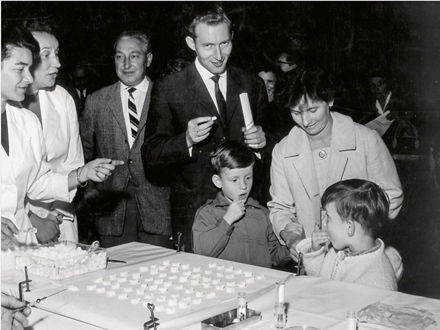 Children and adults stand in line and receive sugar cubes with polio vaccine.